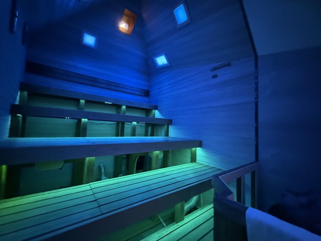 サーマルクライムスタジオ富士のメインサウナ「タワーサウナ・イカロス」の内部。青と緑の幻想的なカラーライティングに照らされた、スタジアムのように幾層にも重なる高い木組みのベンチ。