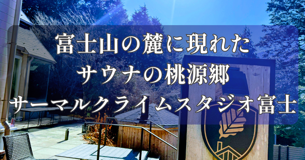 晴れた日の富士山の麓、自然豊かな森の中に立つ、サーマルクライムスタジオ富士の看板と休憩用の椅子。看板にはロゴマークがあり、文字で「富士山の麓に現れたサウナの桃源郷、サーマルクライムスタジオ富士」と書かれている。