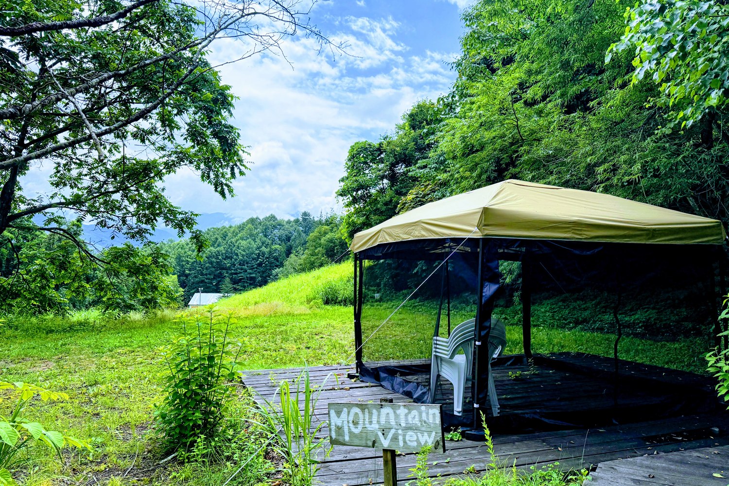 しらかばサウナのマウンテンビューエリア。タープと蚊帳に覆われたウッドデッキの休憩スペースから山々を望む