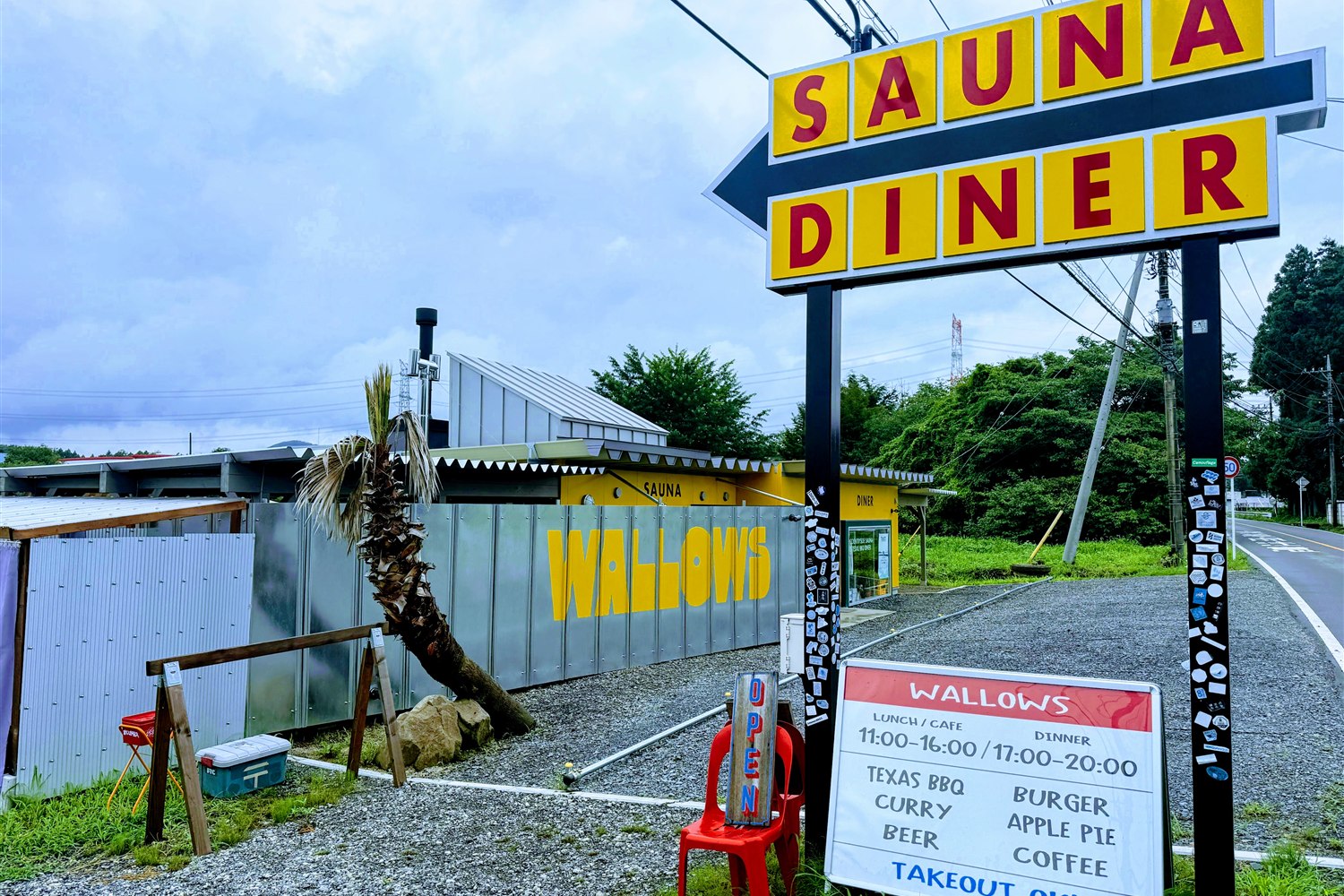 WALLOWS sauna & dinerの外観。黄色い「SAUNA DINER」の大きな看板とWALLOWSのロゴ、メニュー看板