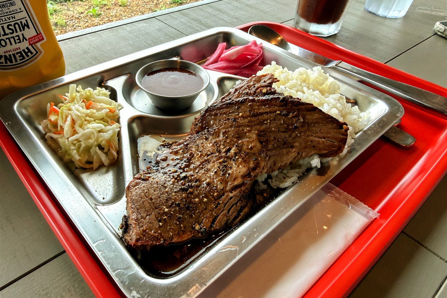 WALLOWS sauna & dinerのテキサスBBQ。薪で燻したブリスケットとライス、コールスロー、BBQソースがトレーに盛られている