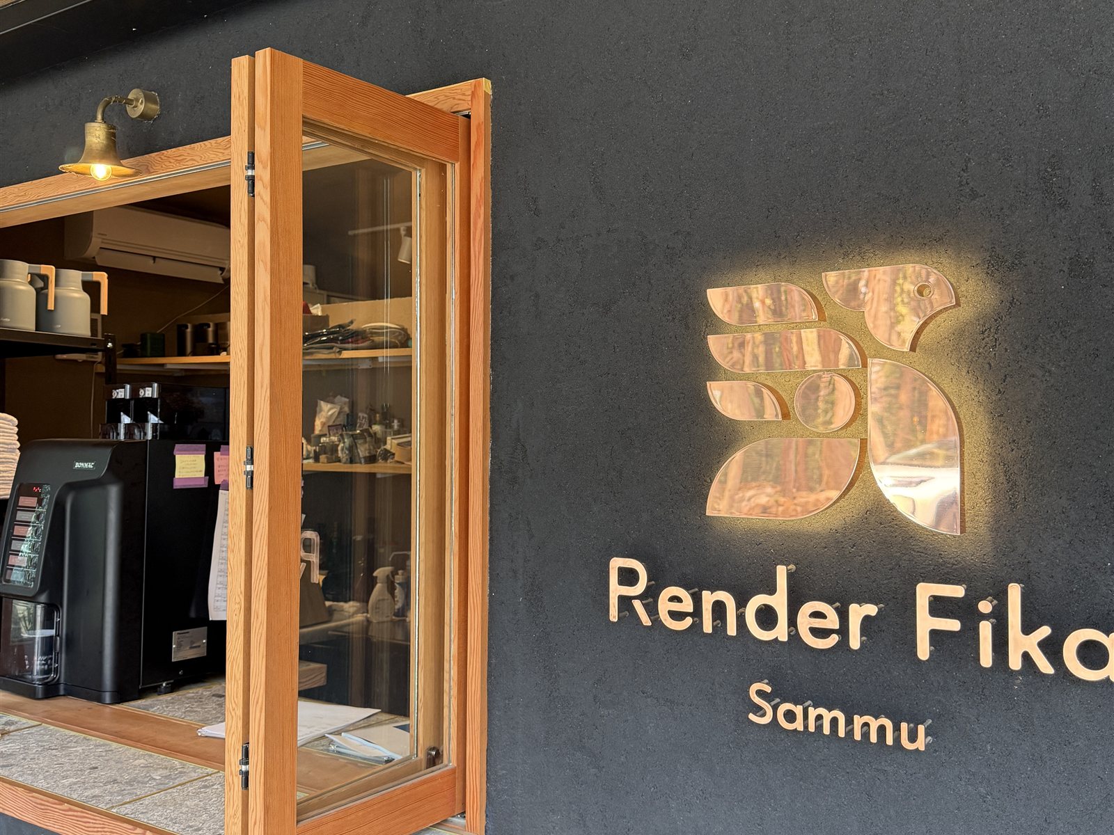 Render Fika Sammuの受付。黒い壁にゴールドで浮かぶ「Render Fika Sammu」のロゴと、木枠のショーケース