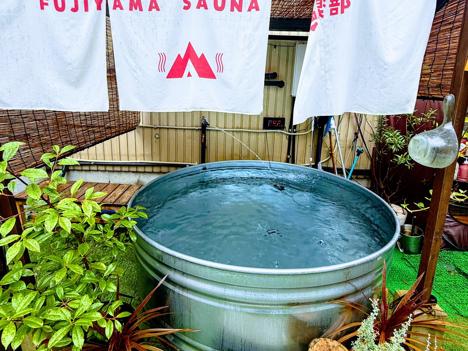 FUJIYAMA SAUNA倶楽部の水風呂。大きめの金ダライ型の水風呂とFUJIYAMA SAUNAの暖簾