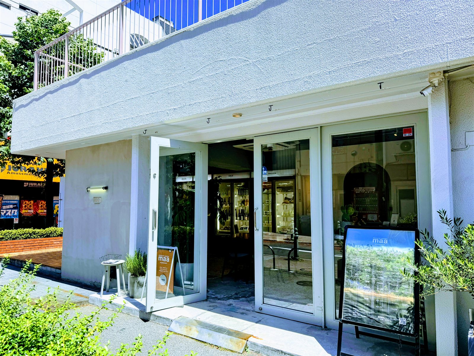 PRIVATE SAUNA maa & GROCERYの外観。白い建物のガラス張りで、グロッサリーの棚とボトルが並ぶ王子の店舗