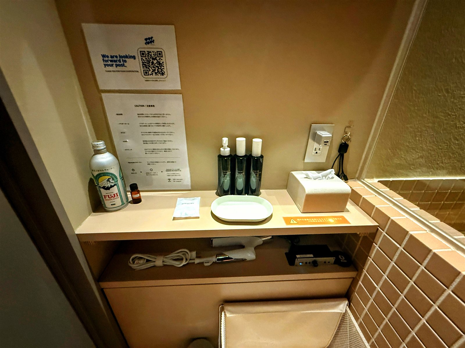 PRIVATE SAUNA maa & GROCERYのアメニティ棚。FUJIミネラルウォーターのボトル、アロマ、スキンケア類、ティッシュ、ドライヤー