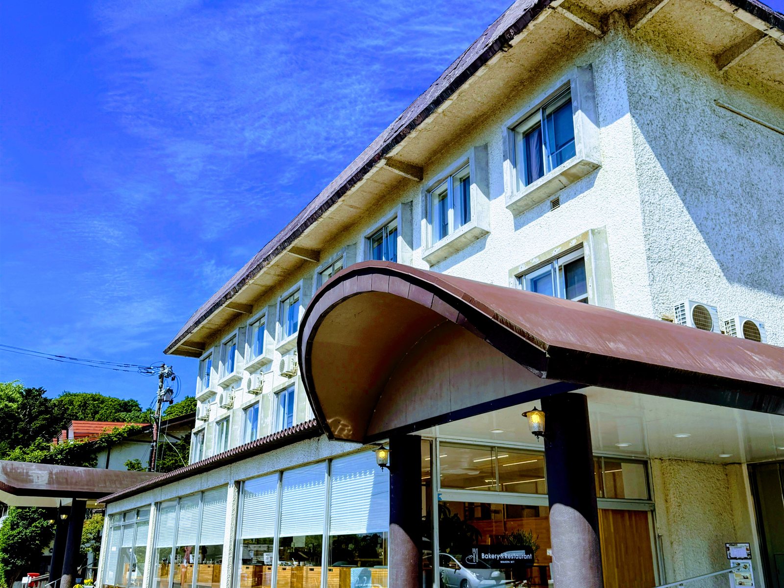 LAKE SIDE HOTEL MINATOYA（ホテルみなとや）の外観。青空の下、Bakery&Restaurantの看板が見える白い建物