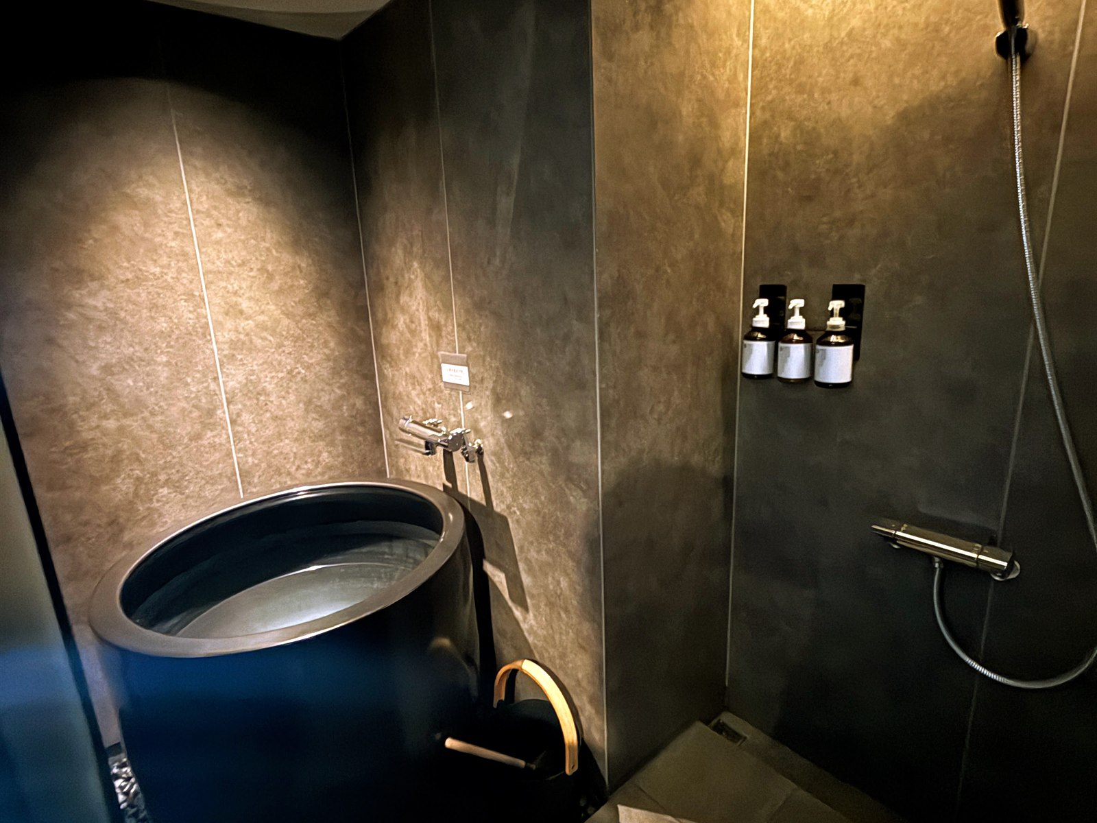 SAUNA OOO SAPPOROの水風呂。1人用の黒い壺型の浴槽とシャワースペース