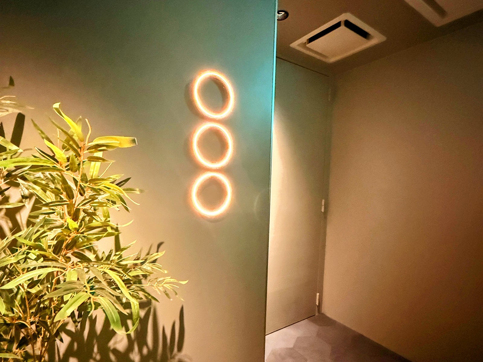 SAUNA OOO SAPPOROの入口。壁に3つの円「○○○」が灯るロゴサインと観葉植物