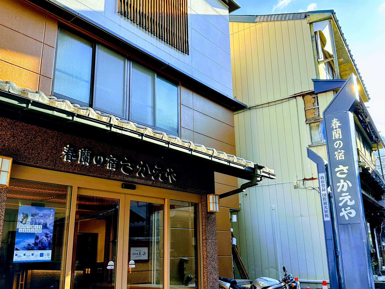 春蘭の宿さかえやの外観。「春蘭の宿さかえや」の看板と政府登録国際観光旅館の表示、青空