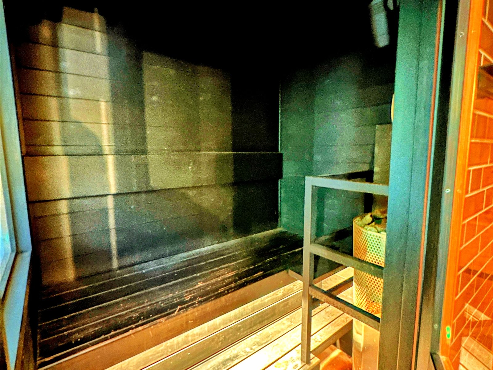 春蘭の宿さかえやの貸切サウナ室内部。黒を基調とした落ち着いた空間に、段状のベンチとサウナストーンのストーブ