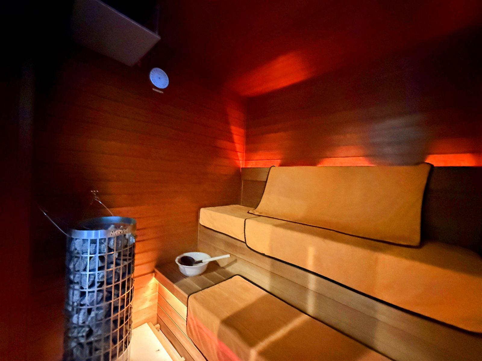 PRIVATE SAUNA S-LIFEのサウナ室内部。HARVIAの円柱型電気ストーブとサウナストーン、2段のベンチにクッション、ロウリュ用のラドルと桶
