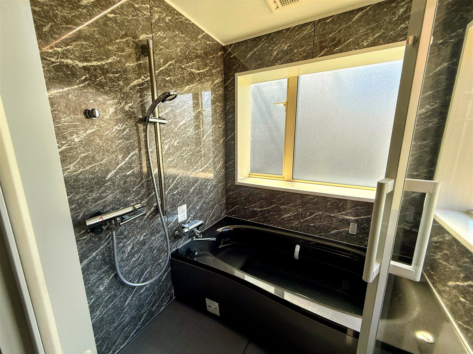 PRIVATE SAUNA S-LIFEの水風呂。黒い大理石調の浴槽と、大きめの曇りガラス窓から光が差し込む明るい浴室
