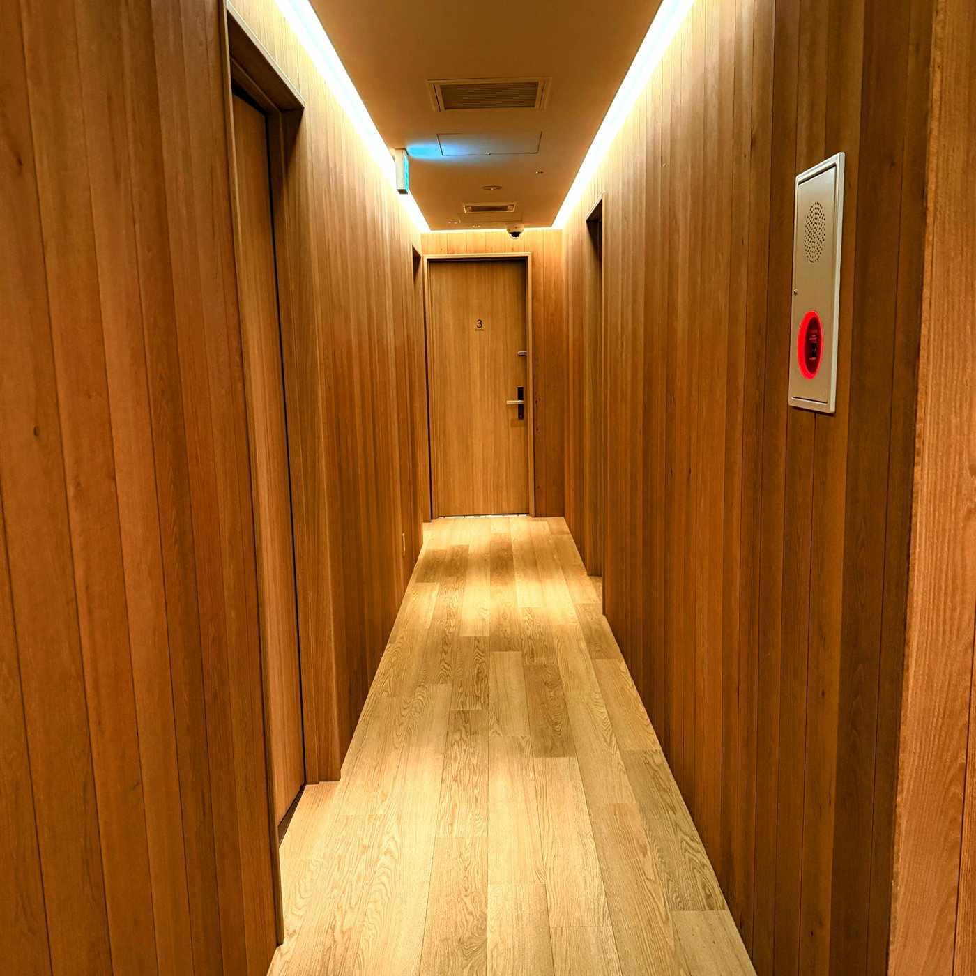 yksi SAUNA & STAYの木目に統一された廊下。間接照明が灯り、個室サウナのドアが並んでいる