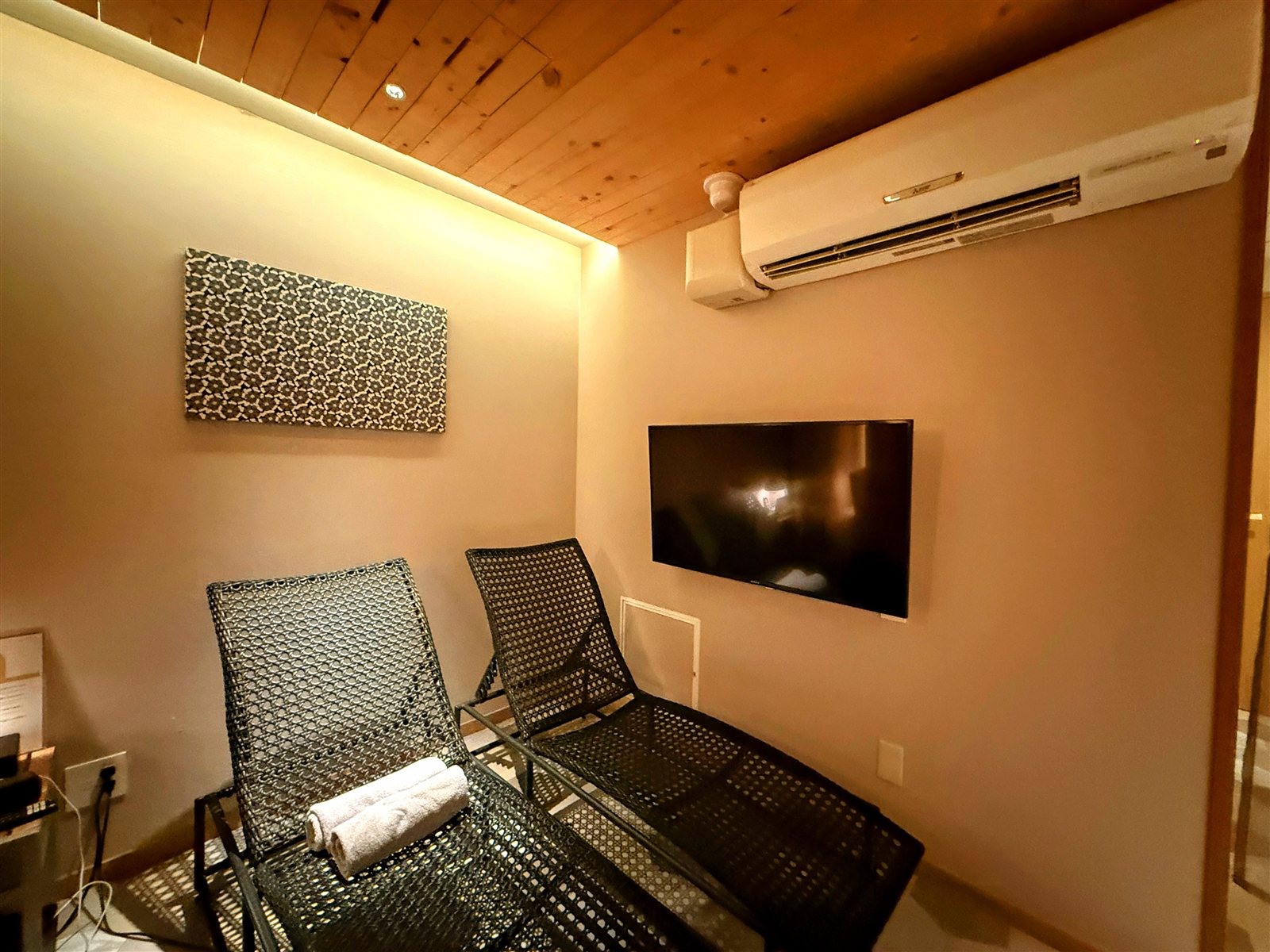 yksi SAUNA & STAYの休憩スペース。壁掛けのテレビとエアコン、デッキチェアが備えられた快適な個室空間