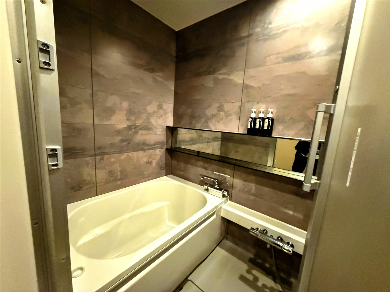 yksi SAUNA & STAYの個室内の水風呂。大理石調の壁に囲まれた白い浴槽（ユニットバス）に水を張るスタイル