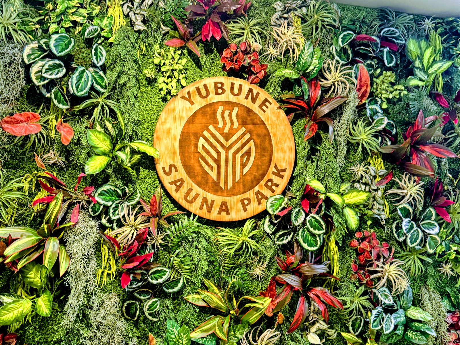 YUBUNE SAUNA PARKのグリーンウォール。色とりどりの植物の中央に「YUBUNE SAUNA PARK」の木製ロゴ