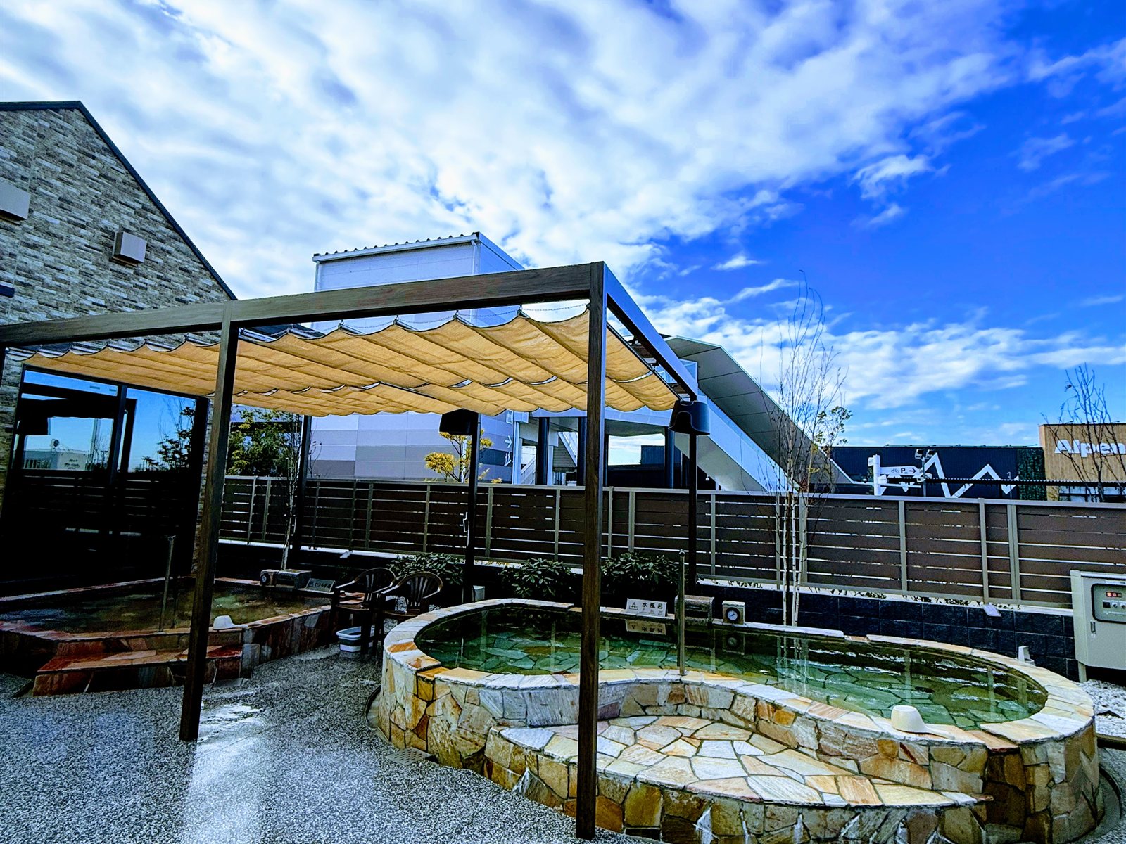 YUBUNE SAUNA PARKの露天エリア。石造りの丸い水風呂とタープの日除け、青空が広がる開放的な空間