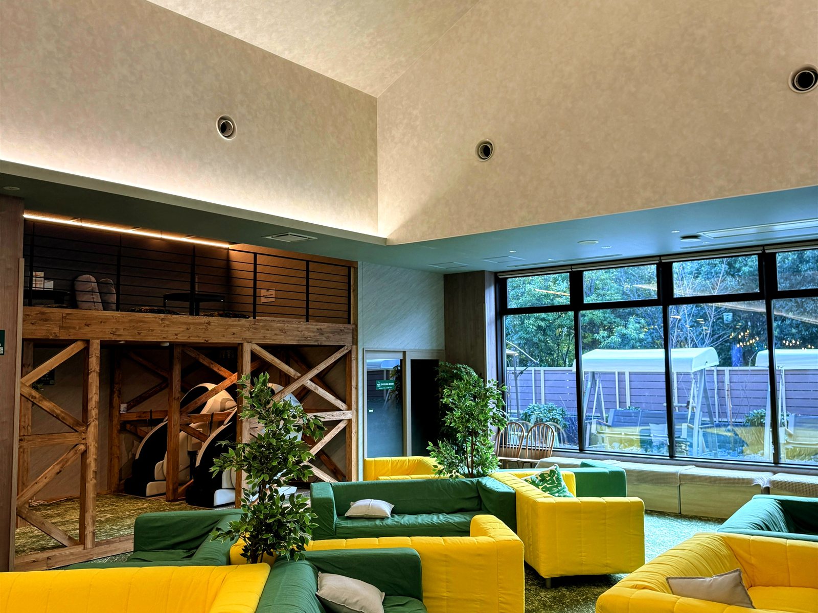 YUBUNE SAUNA PARKの館内ラウンジ。黄色と緑のカラフルなソファ、観葉植物、大きな窓、奥にととのいスペースのブース