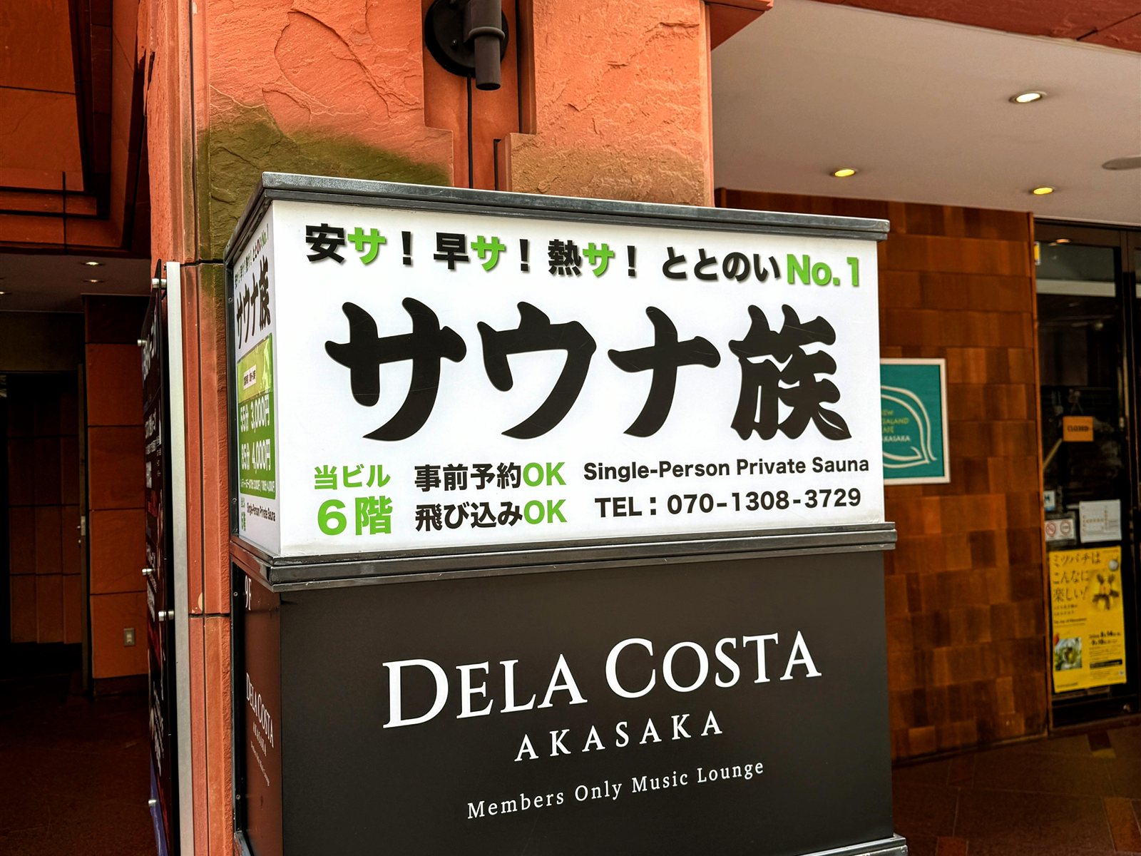 サウナ族の入口看板。「安サ！早サ！熱サ！ととのいNo.1 サウナ族 Single-Person Private Sauna 当ビル6階」と書かれた赤坂のビル