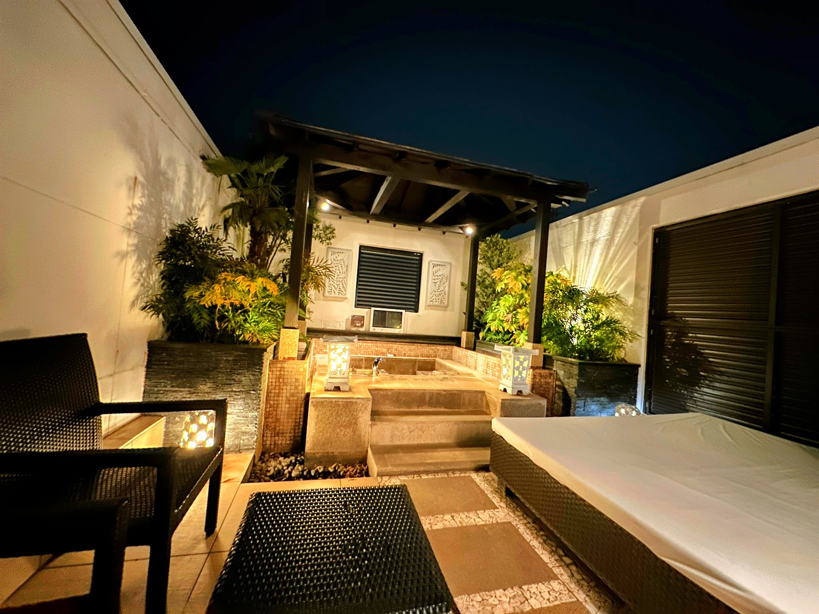 HOTEL SEEDS 桶川店の夜の屋上露天風呂と外気浴スペース。ライトアップされた東屋とチェア
